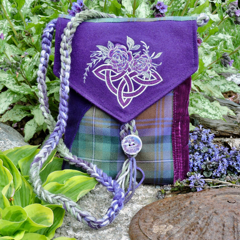 Purple bag with floral design and tartan pattern, surrounded by greenery and flowers.
